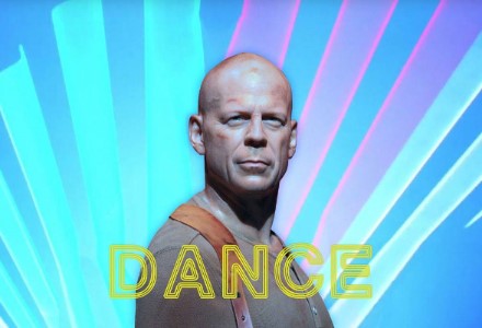Bruce Willis, bruised and scratched, stares out at the camera in front of a bright blue and purple background